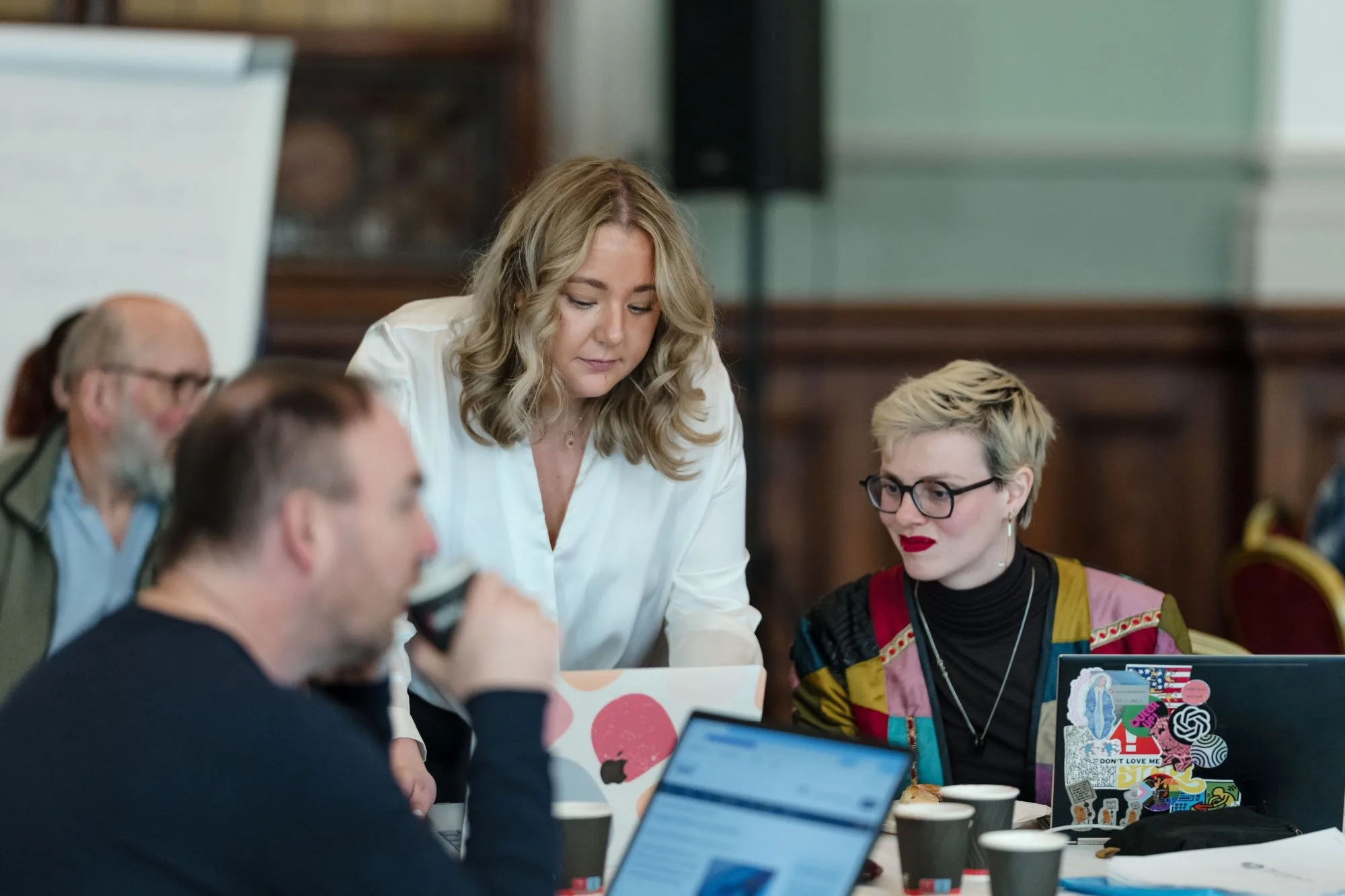 People at a table during a session, with coffee and laptops.